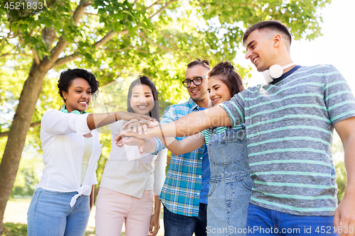 Image of happy smiling friends stacking hands in park