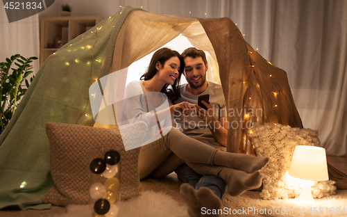 Image of happy couple with smartphone in kids tent at home