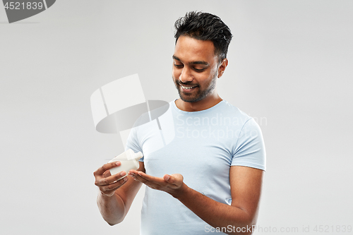 Image of happy indian man applying lotion to his hand