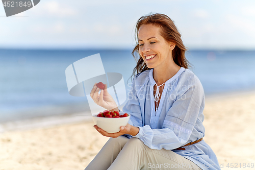 Image of happy woman eating strawberries on summer beach