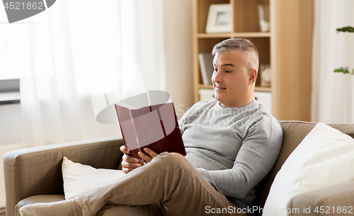 Image of man sitting on sofa and reading book at home