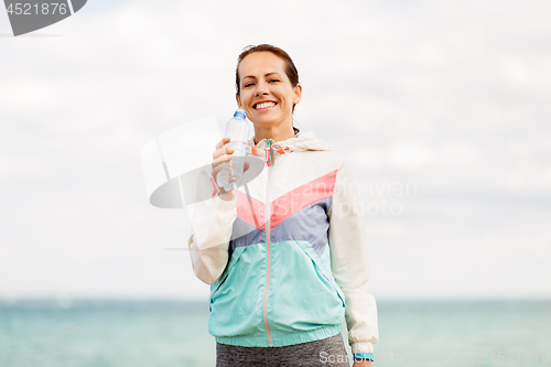 Image of woman drinking water after exercising at seaside