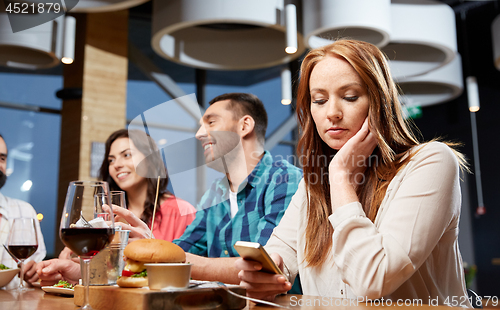 Image of bored woman messaging on smartphone at restaurant