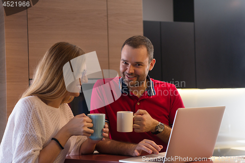 Image of couple drinking coffee and using laptop at home