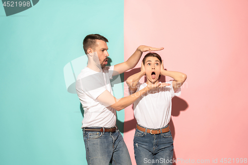 Image of Closeup portrait of young couple, man, woman. TV fan concept on pink and blue background. Emotion contrasts