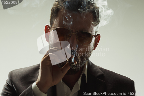 Image of The barded man in a suit holding cigar