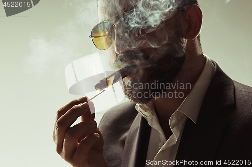 Image of The barded man in a suit holding cigar