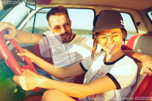 Image of Laughing romantic couple sitting in car while out on a road trip at summer day