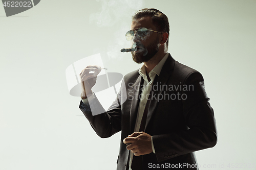 Image of The barded man in a suit holding cigar