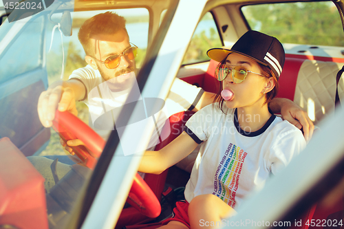 Image of Laughing romantic couple sitting in car while out on a road trip at summer day