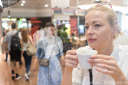 Image of Portrait of a casual young blond woman having a cup of coffee, sitting in cafe indoors of an airport, station, food market or shopping mall.