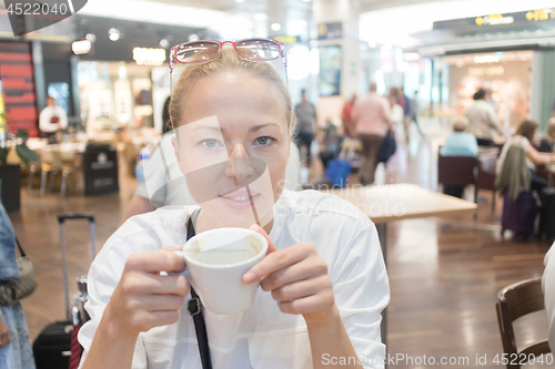 Image of Portrait of a casual young blond woman having a cup of coffee, sitting in cafe indoors of an airport, station, food market or shopping mall.