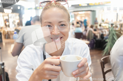 Image of Portrait of a casual young blond woman having a cup of coffee, sitting in cafe indoors of an airport, station, food market or shopping mall.