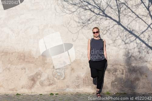 Image of Graphical and textured artisic image of modern trendy fashionable woman wearing sunglasses leaning against old textured retro wall with tree shadow falling on the wall.