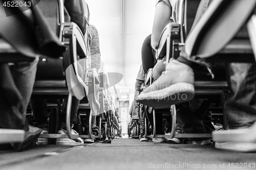 Image of Low agle view of passenegers commercial airplane aisle with passenegers sitting on their seats while flying. Black and white photo.