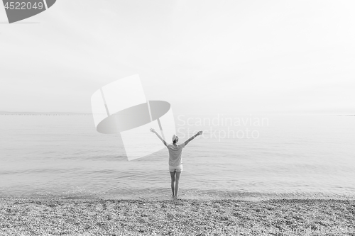 Image of Happy Carefree Woman Enjoying Sunset Walk on White Pabbled Beach.