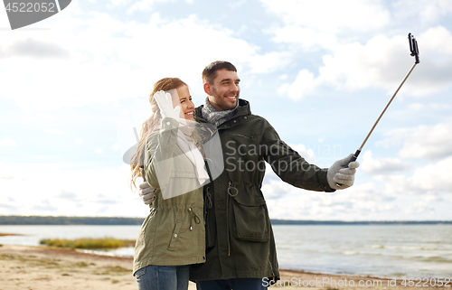 Image of happy couple taking selfie on beach in autumn