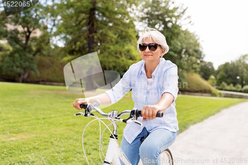 Image of happy senior woman riding bicycle at summer park