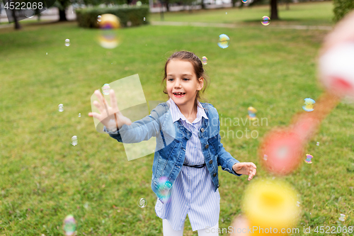 Image of happy girl playing with soap bubbles at park