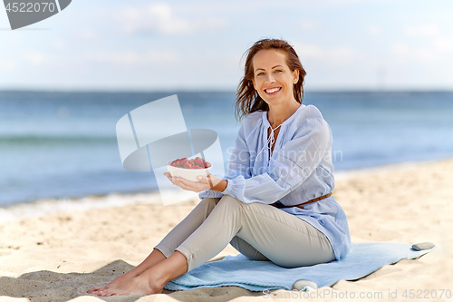 Image of woman holding bowl with strawberries on beach