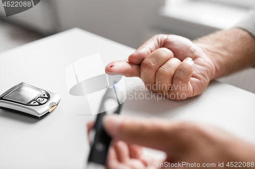 Image of senior man with glucometer checking blood sugar