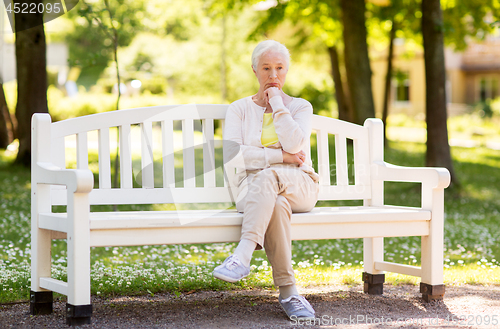 Image of sad senior woman sitting on bench at summer park