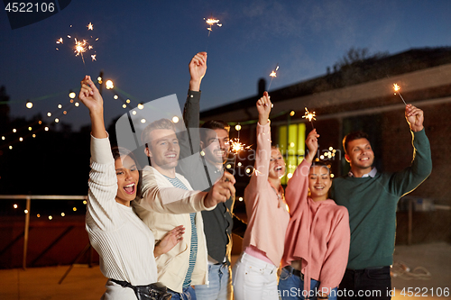 Image of happy friends with sparklers at rooftop party