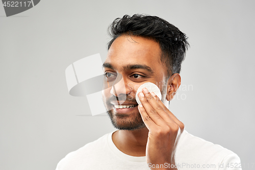 Image of smiling indian man cleaning face with cotton pad