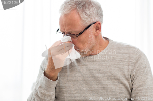 Image of sick senior man with paper wipe blowing his nose