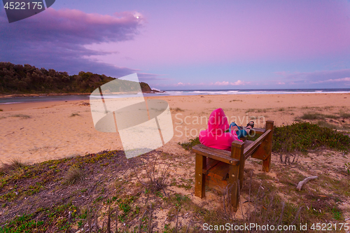 Image of Woman relaxes on bench overlooking beach in the afternoon dusk