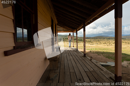 Image of Woman standing on verandah of rural timber homestead in snowy high plains