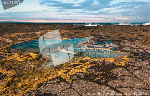 Image of Female leisurely floating in a rock pool by the ocean