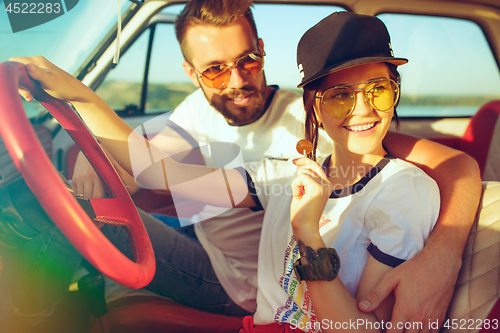 Image of Laughing romantic couple sitting in car while out on a road trip at summer day