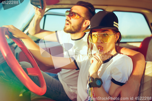 Image of Laughing romantic couple sitting in car while out on a road trip at summer day