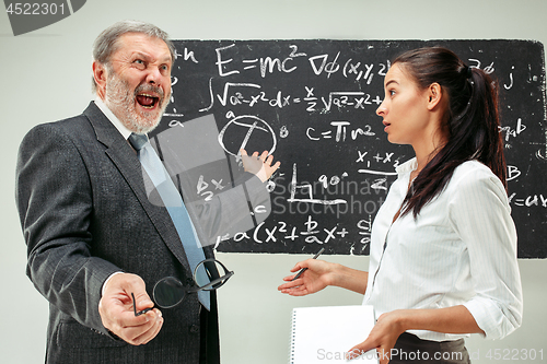 Image of Male professor and young woman against chalkboard in classroom