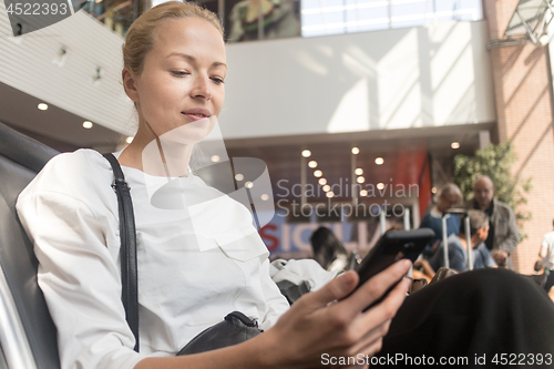 Image of Female traveler reading on her cell phone while waiting to board a plane at departure gates at airport terminal.