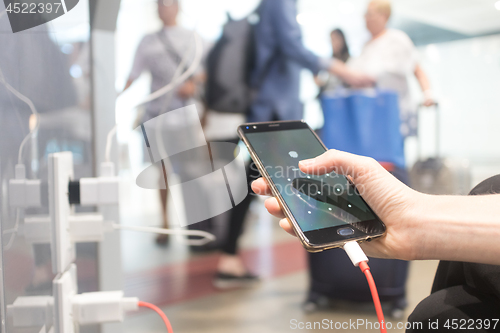 Image of Female hands holding and using smartphone while charging it in a public place using electric plug and a charging cable