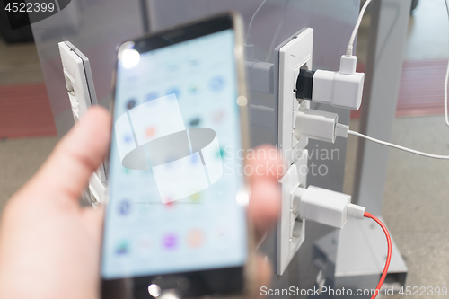 Image of Female hands holding cell phone and using smartphone apps while charging it in a public place using electric plug and a charging cable. Focus on charging adapter.