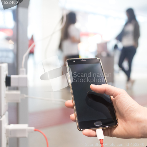 Image of Female hands holding and using smartphone while charging it in a public place using electric plug and a charging cable