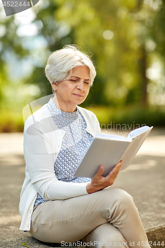 Image of senior woman reading book at summer park