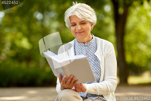 Image of senior woman reading book at summer park