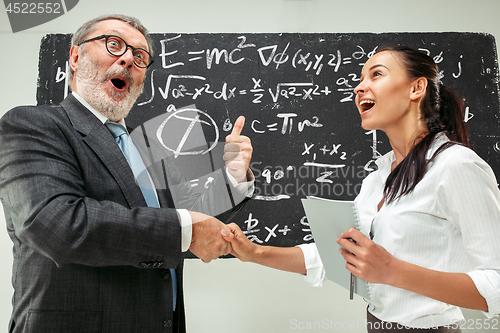 Image of Male professor and young woman against chalkboard in classroom