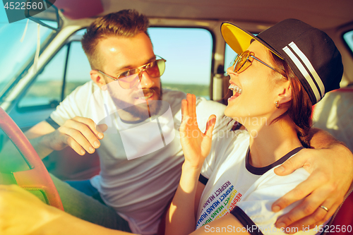 Image of Laughing romantic couple sitting in car while out on a road trip at summer day