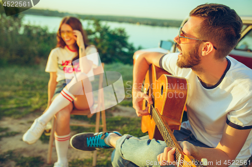 Image of Couple sitting and resting on the beach playing guitar on a summer day near river