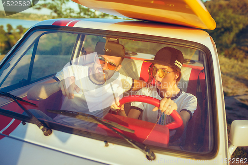 Image of Laughing romantic couple sitting in car while out on a road trip at summer day