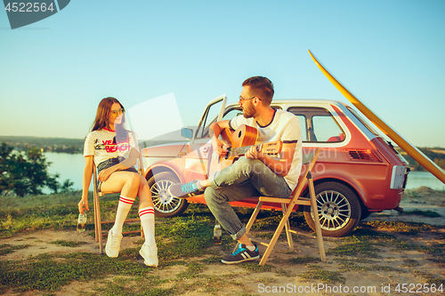 Image of Couple sitting and resting on the beach playing guitar on a summer day near river