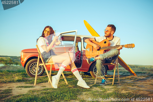 Image of Couple sitting and resting on the beach playing guitar on a summer day near river