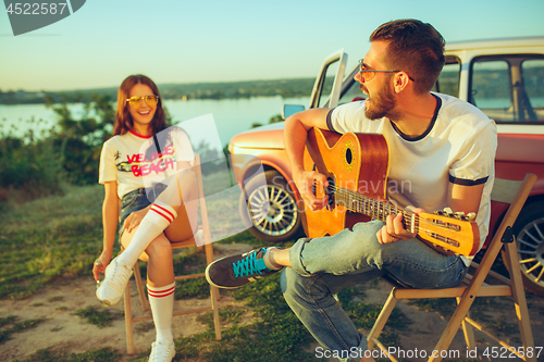 Image of Couple sitting and resting on the beach playing guitar on a summer day near river