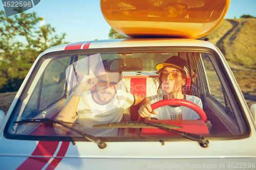 Image of Laughing romantic couple sitting in car while out on a road trip at summer day