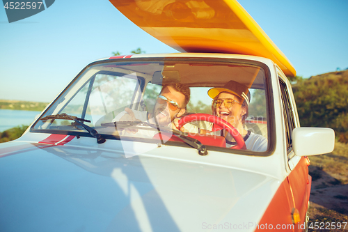 Image of Laughing romantic couple sitting in car while out on a road trip at summer day